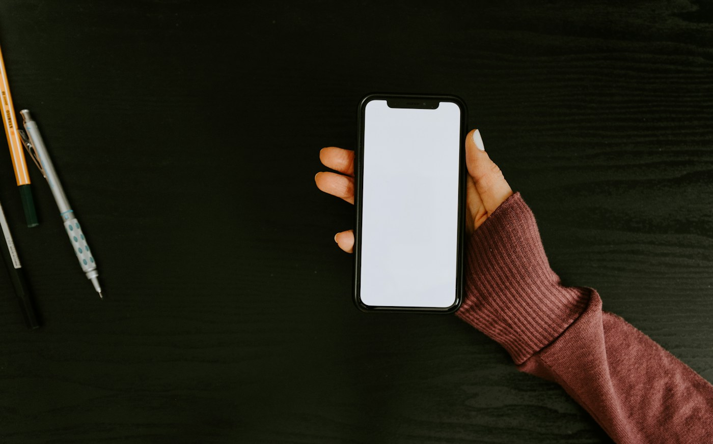 机の上でスマートフォンを手に取り、画面を確認する手元。